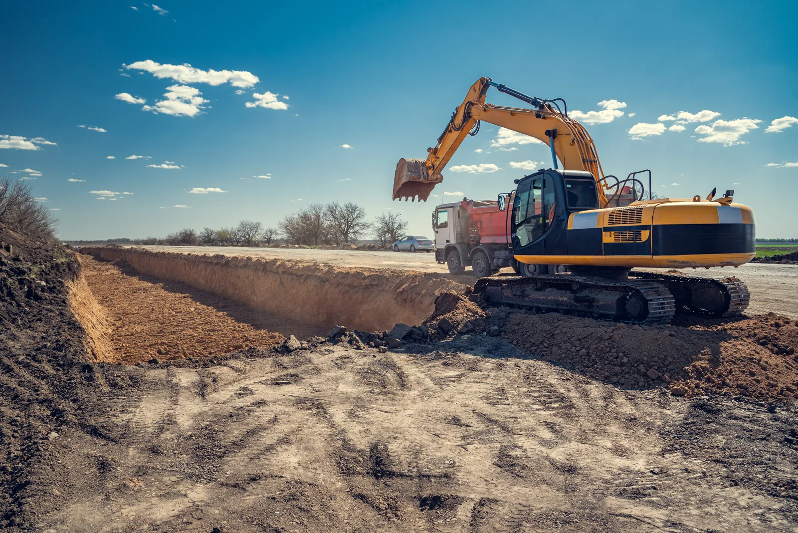Excavator loading a dump truck beside a large excavation.
