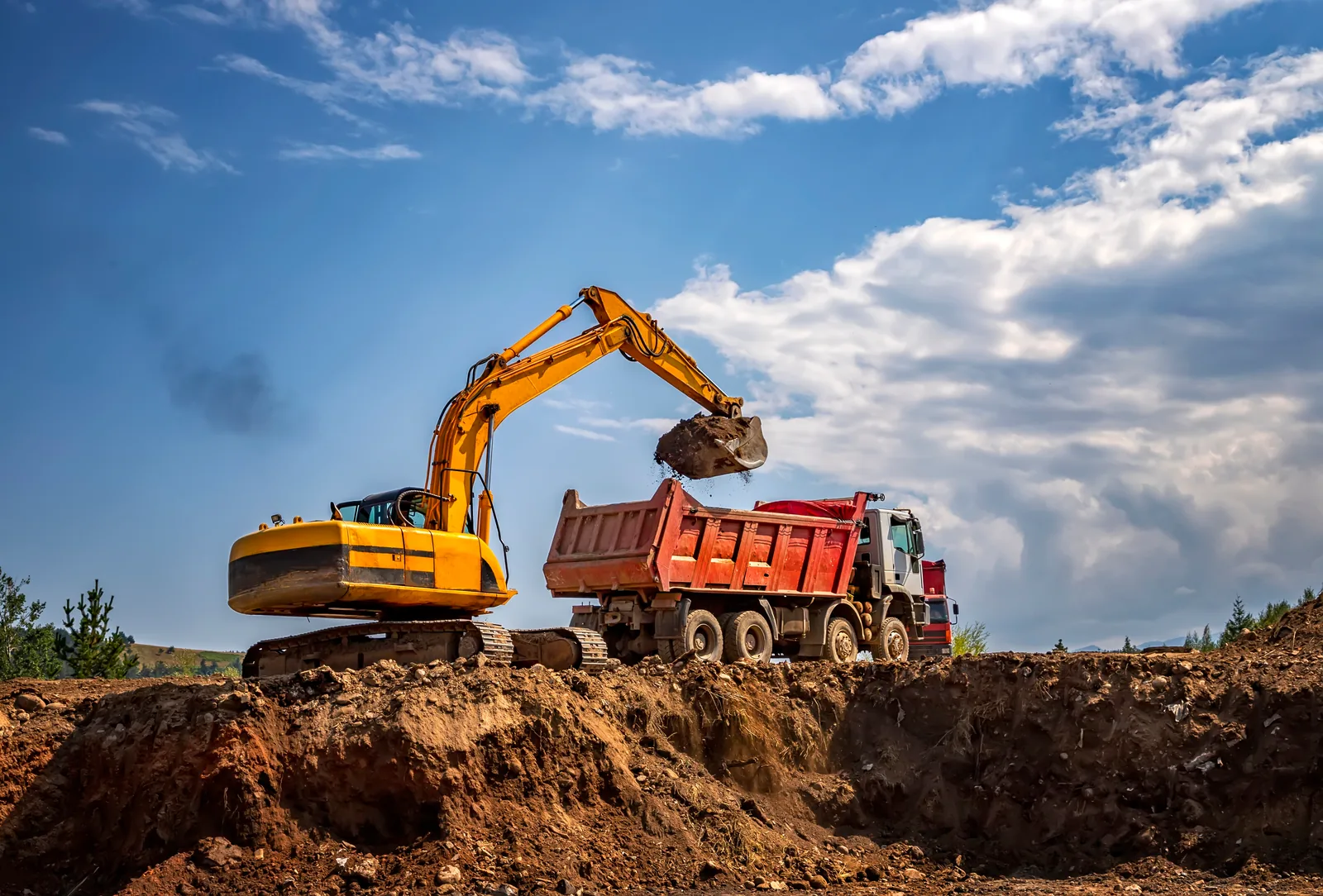 Excavator loading soil into a red dump truck.